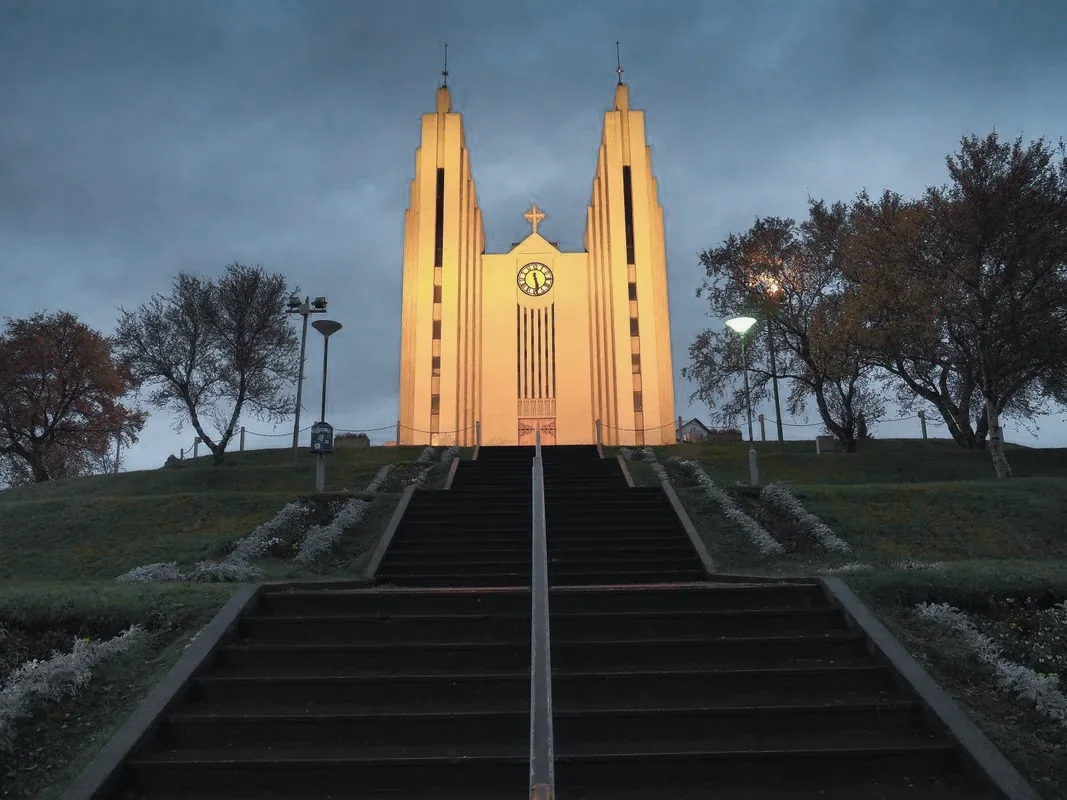Akureyrarkirkja lit at dusk above the steps from the town centre